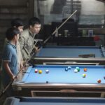 a group of men standing around a pool table